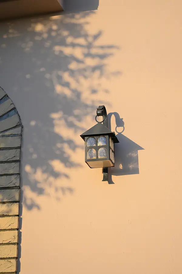 “夕陽の木漏れ日で、玄関ランプの影が壁に落ちる情景”